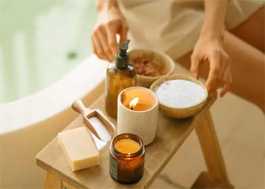 A girl sitting on the bathtub edge by a bowl of sugar and hygiene products. 