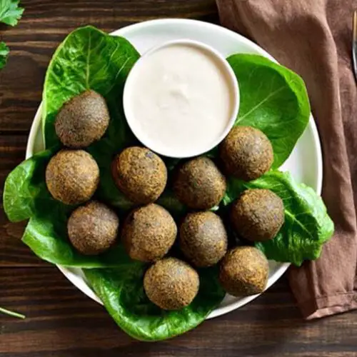 Top view of rich vegan Himalayan Tartary Buckwheat falafel balls on a bed of greens and by a cup of creamy vegan Ranch dip.