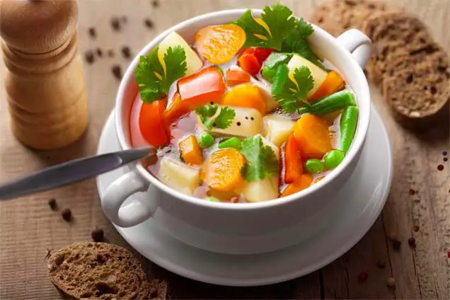 Top view of chunky vegan vegetable soup and whole grain bread.