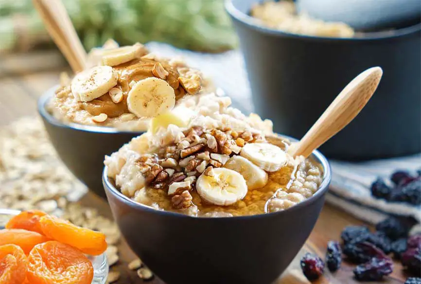 Close on a stacked bowl of delicious quinoa breakfast porridge topped with fresh sliced bananas, walnuts, and organic date syrup.