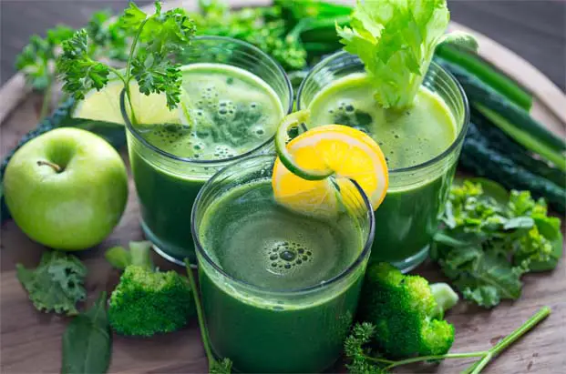 Three glasses of chlorella green juice by  broccoli, kale, lemon, an apple, celery, parsley. 