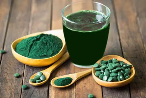 Spirulina drink, powder, and tablets on a wooden board. 