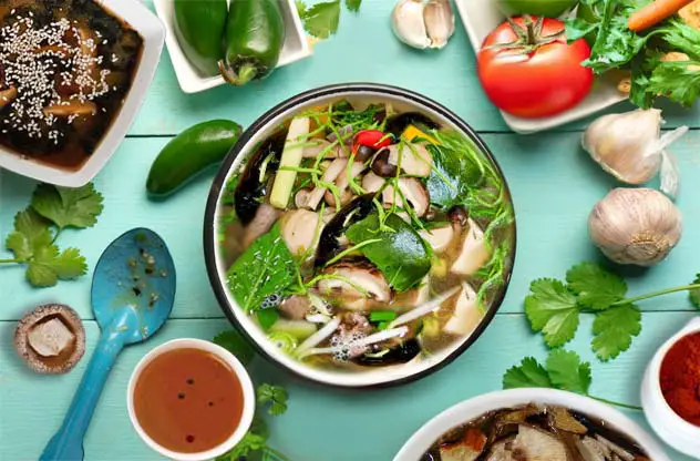 Top view of large bowl of vegan bone broth surrounded by veggies ad herbs.