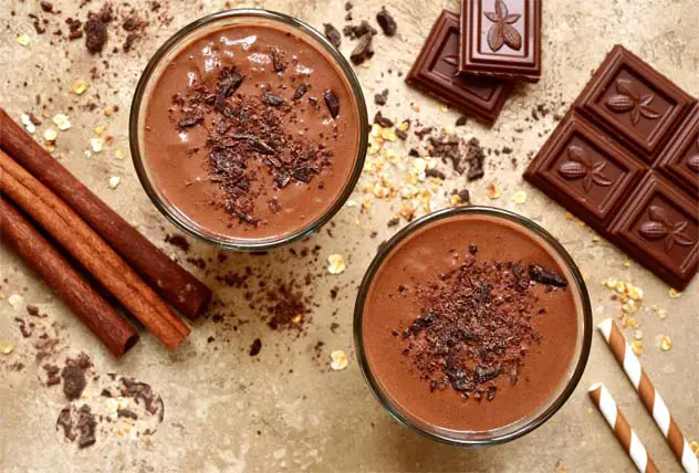 Top view of rich vegan chocolate milkshakes with cacao nibs, chocolate chunks, and cinnamon sticks.