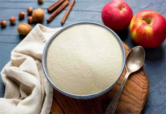 Top view of a bowl of agar powder by huge ripe apples, nuts, and cinnamon sticks.