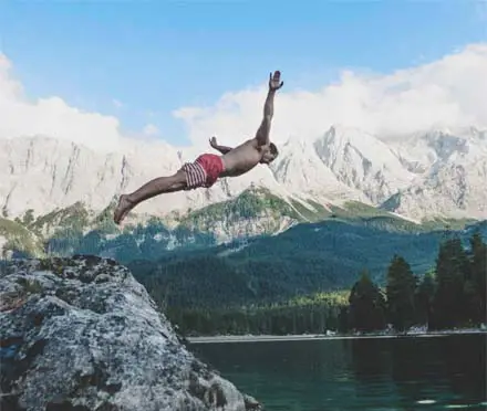 A man diving off a rock into a freezing cold mountain lake.