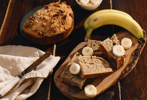 Top view of sliced Himalayan Tartary Buckwheat banana bread with fresh bananas and a round loaf.