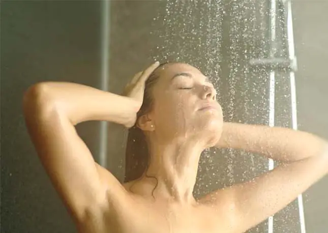 A girl tilting her head back in a cold shower.