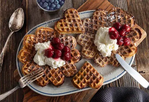 Top view of heart-shaped Himalayan Tartary Buckwheat waffles topped with cherries and vegan whipped topping.