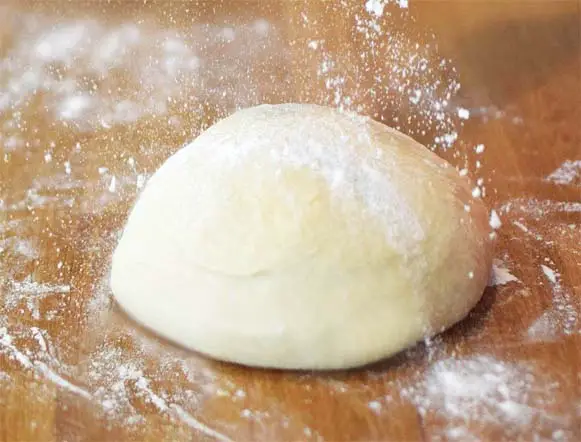 Mound of leavened pizza dough on a floured board. 