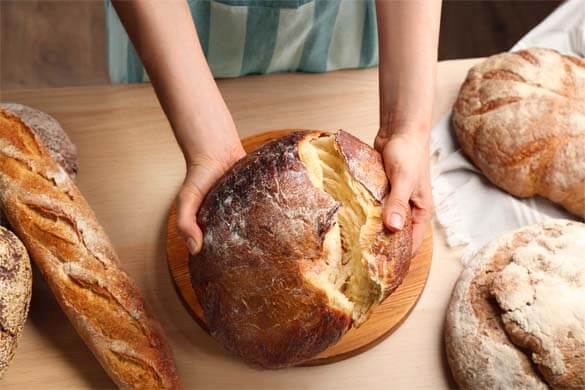 Close-up of girl's hands holding a fresh loaf of buckwheat sourdough bread among other homemade loaves and baguettes. 