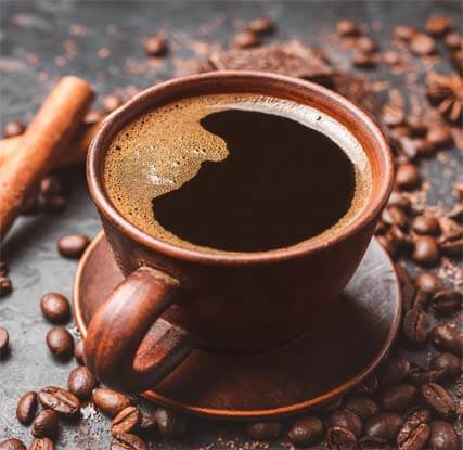 Rustic mug of dark infrared coffee surrounded by cinnamon, cacao, and coffee beans.