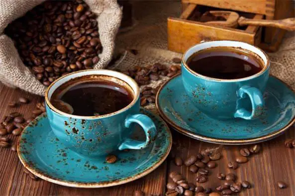 Two aqua artisan mugs of infrared coffee beside an open bag of beans and wooden storage box.