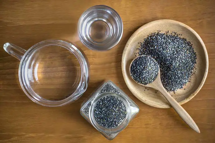 Top view of chia seeds in a bowl, spoon, and jar beside a glass and pitcher of water.