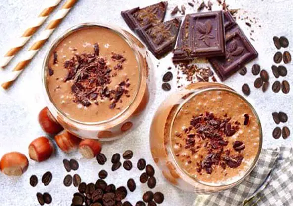 Top view of rich chocolate coffee protein smoothies surrounded by coffee beans, hazelnuts, and dark chocolate chunks.