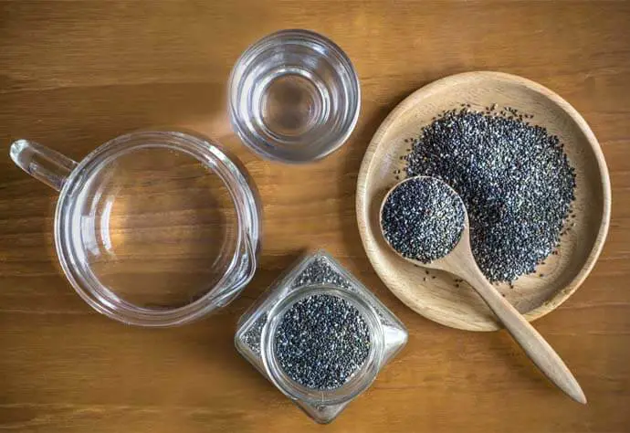 Top view of chia seeds in a bowl, spoon, and jar beside a glass and pitcher of water.