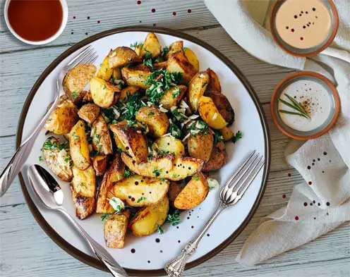 Top view of scrumptious spiced potato wedges on a plate with three different dips.    