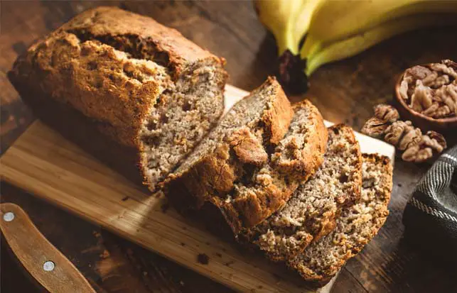 Rich loaf of Himalayan Tartary Buckwheat banana bread surrounded by nuts and bananas.