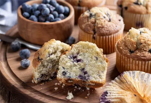 Himalayan Tartary Buckwheat blueberry muffins by a bowl of blueberries on a board.