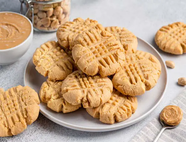 Plate of rich vegan peanut butter cookies with Himalayan Tartary Buckwheat by a bowl of peanut butter and jar of shelled peanuts.