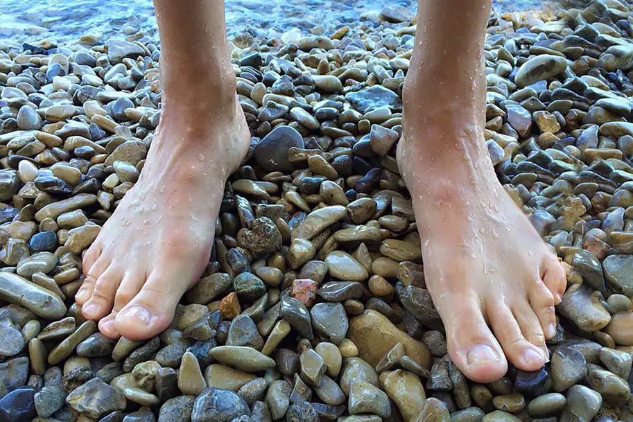 Close on a pair of bare wet feet grounding on a bed of shimmery river rocks.