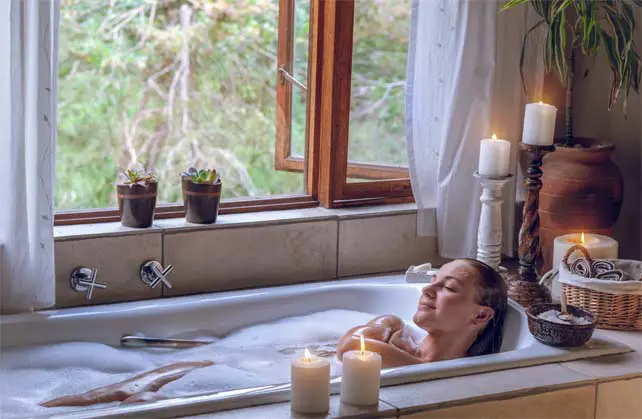 A girl enjoying a deliciously relaxing Epsom salt soak by candlelight and a picturesque window. 