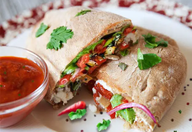 Sliced vegan buckwheat calzone on a plate with veggie filling and marinara dip. 