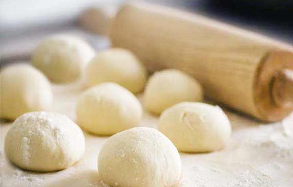 Balls of Himalayan Tartary Buckwheat calzone dough by a rolling pin on a floured board.
