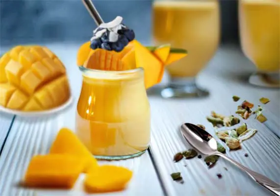 Glasses of delicious vegan mango smoothie with HTB Rejuvenate Superfood topped by mango slices, blueberries, and coconut.