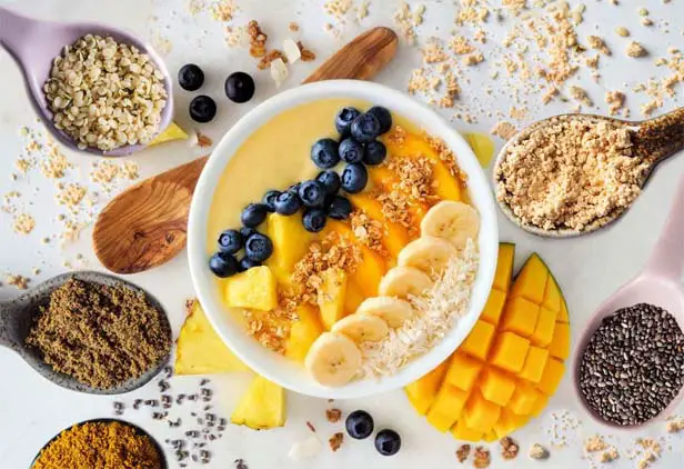 Top view of vegan mango smoothie with HTB Rejuvenate surrounded by spoons of superfoods.