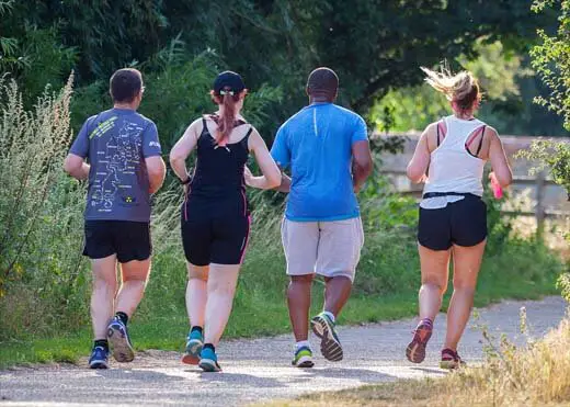 Four overweight people jogging on a scenic path during a weight loss workout.