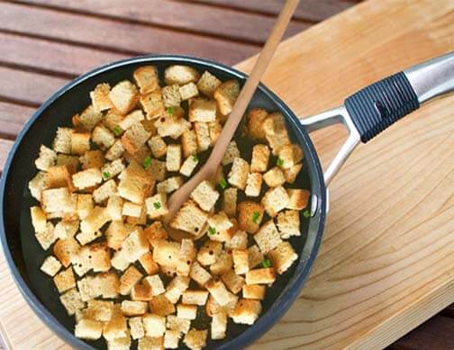 Top view of homemade HTB sourdough garlic croutons in a wok on a board. 