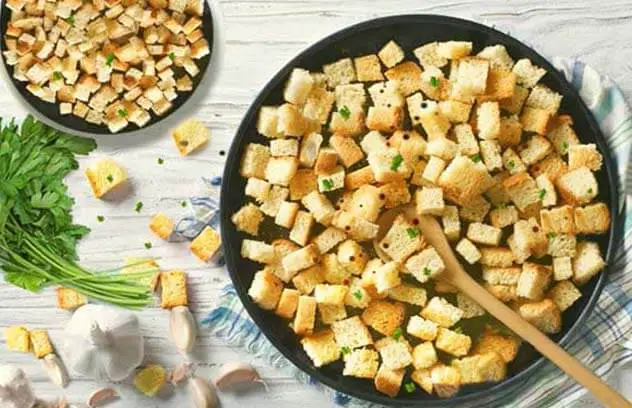 Top view of delicious homemade Himalayan Tartary Buckwheat sourdough garlic croutons in bowls by fresh cut garlic and herbs.