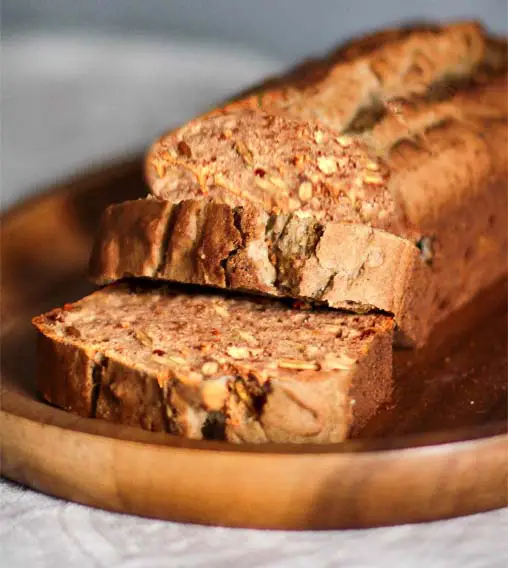 Close-up of a rich and nutty Himalayan Tartary Buckwheat pumpkin bread loaf sliced on a wooden platter. 