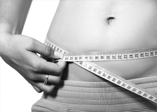 Close-up of a girl measuring her hips and abdomen with a measuring tape. 