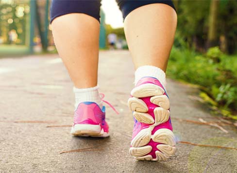 Rear view of a woman's calves and tennis shoes walking on an outdoor sidewalk.  