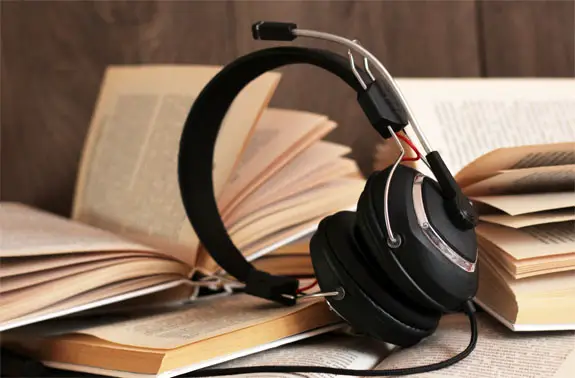 Stacks of hardcover books by headphones on a desk represent audiobooks.