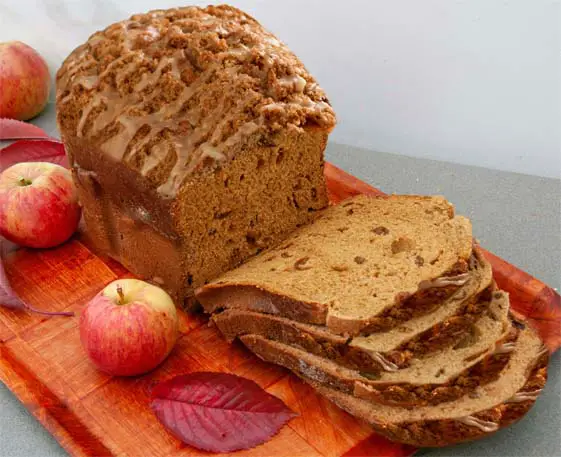 Rich and moist loaf of glazed vegan Himalayan Tartary Buckwheat apple bread sliced on a cutting board by fresh apples and leaves.