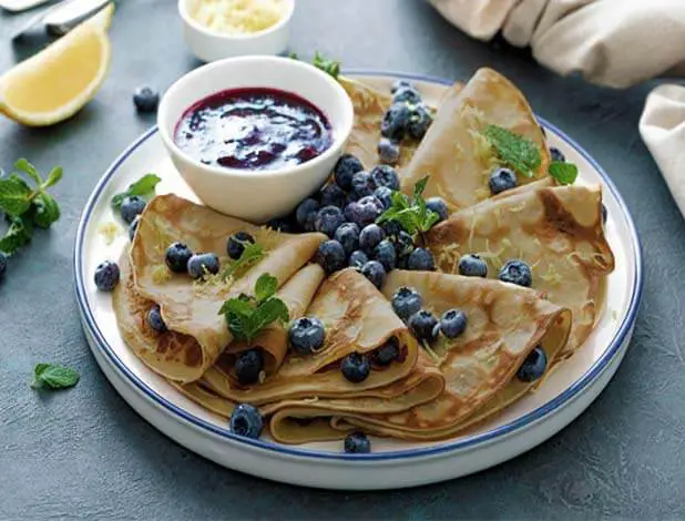 Stacked plate of delectably rich Himalayan Tartary Buckwheat crepes with organic fresh blueberries and coulis.  