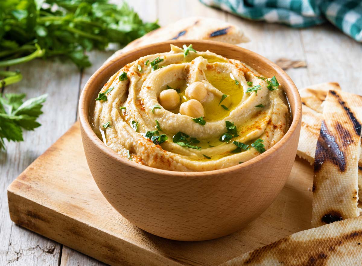 Bowl of delicious homemade hummus on a cutting board with pita bread and fresh herbs.