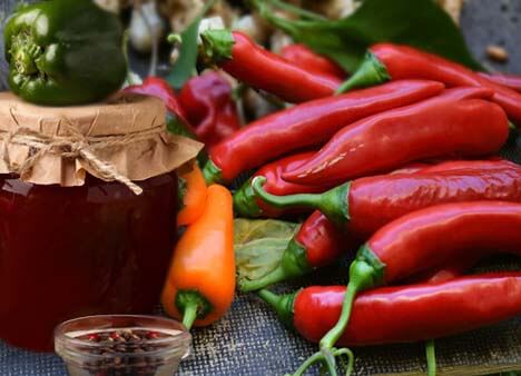 Stacks of red and orange chili peppers  by a decoratively sealed mason jar of hot lava sauce. 