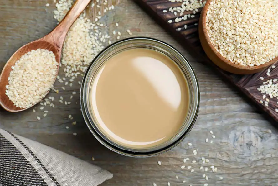 Top view of rich and creamy vegan tahini in a glass bowl by slews of organic sesame seeds.  