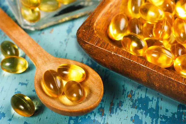 Close-up of vegan omega-3 fatty acid gels in a wooden spoon and saucer on a rustic aqua board.