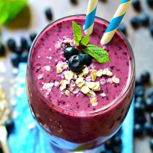 Overview of rich vegan blueberry protein smoothie on a rustic board by fresh ripe blueberries and steel cut oats.