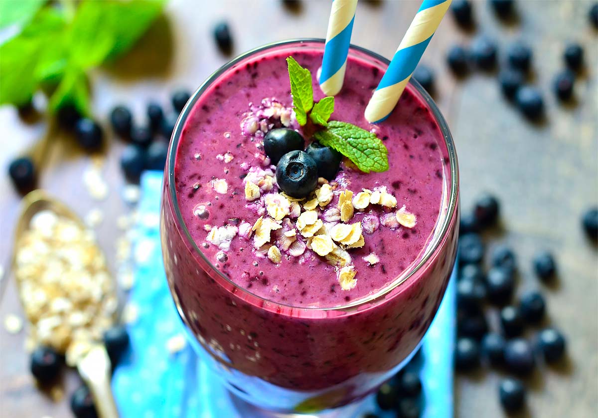 Overview of rich vegan blueberry protein smoothie on a rustic board by fresh ripe blueberries and steel cut oats.