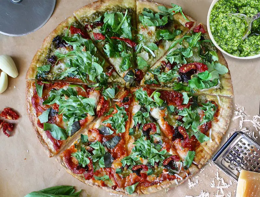 Top view of sliced vegan pizza with Himalayan Tartary Buckwheat crust by pesto, chili peppers, and vegan cheese.