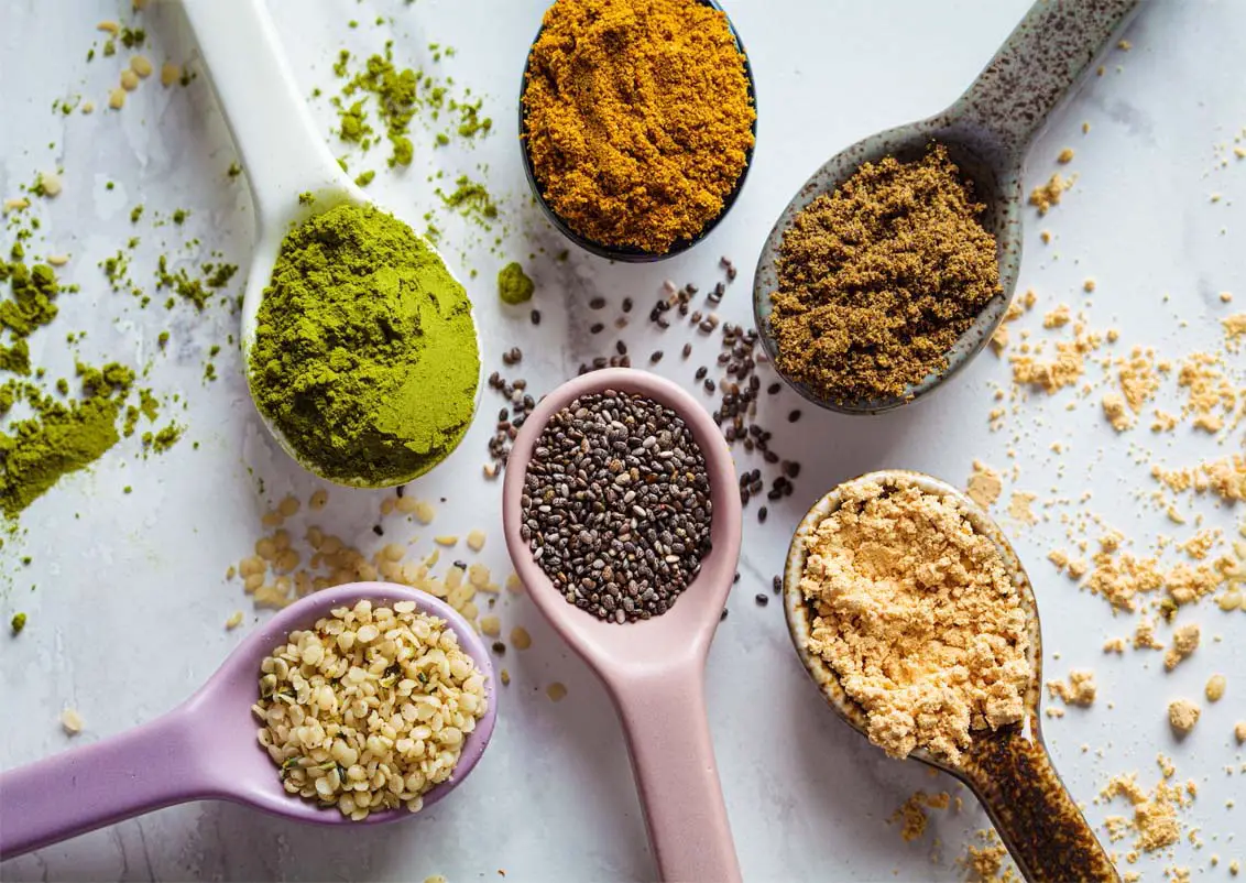 Heaping spoons of assorted superfood powders and chia seeds displayed on a whiteboard.