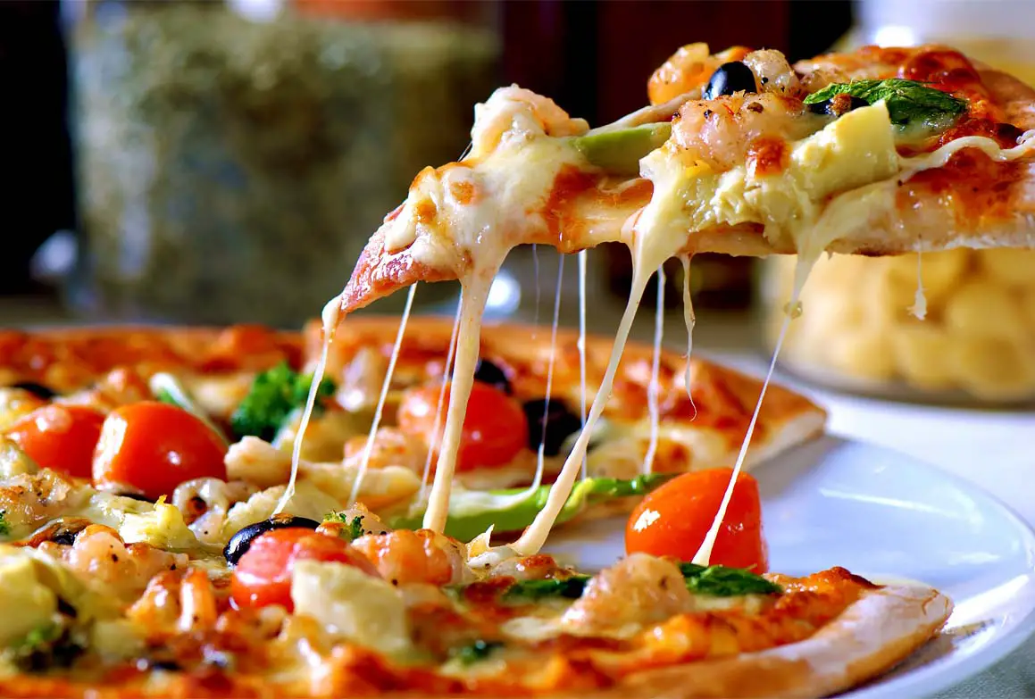 Close-up of a rich slice of vegan pizza being lifted from a plate.  