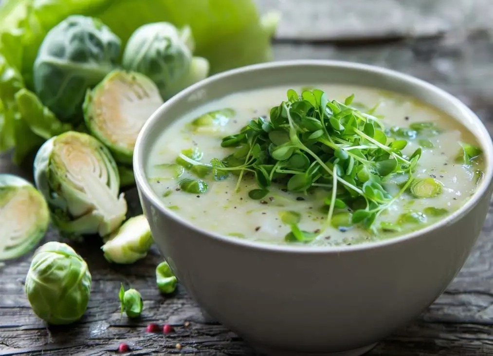 Close-up of rich creamy Brussels sprout soup topped with microgreens on a wooden board.  