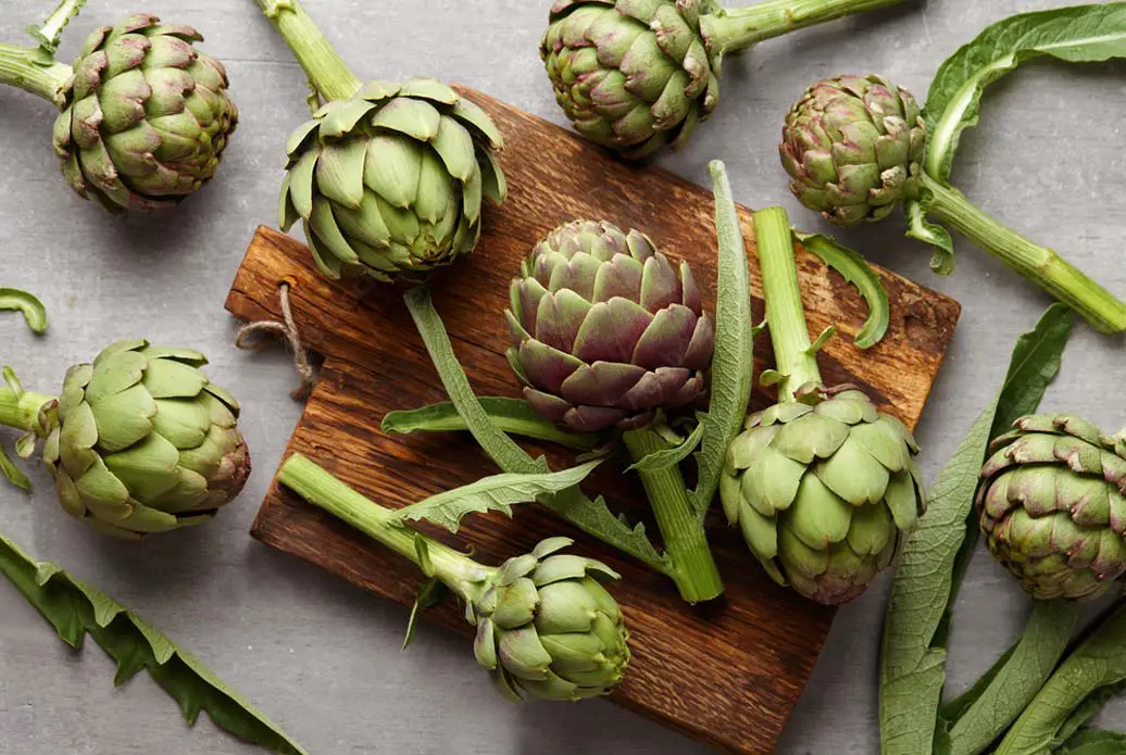 Top view of fresh whole artichokes splayed across a wooden cutting board. 